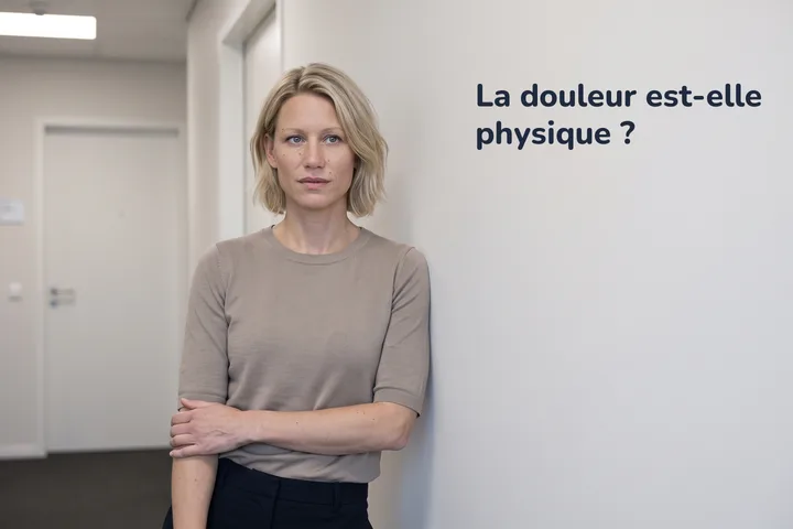La douleur est-elle physique ? — une femme s'arrête dans un couloir de bureau, un avant-bras pressé sur le ventre