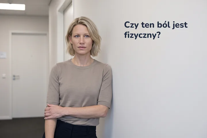 Czy ten ból jest fizyczny? — kobieta przystaje na biurowym korytarzu, z przedramieniem przyciśniętym do brzucha