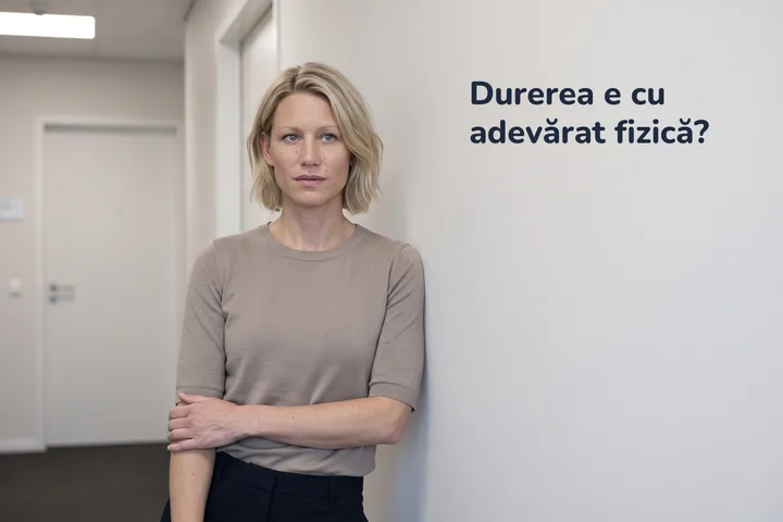 Durerea e cu adevărat fizică? — o femeie se oprește pe un hol de birou, cu antebrațul apăsat pe abdomen