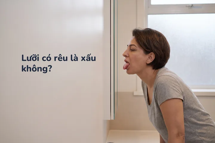 Lưỡi có rêu là xấu không? — một phụ nữ soi gương nhà tắm lúc trời vừa sáng, nhìn cái lưỡi của mình
