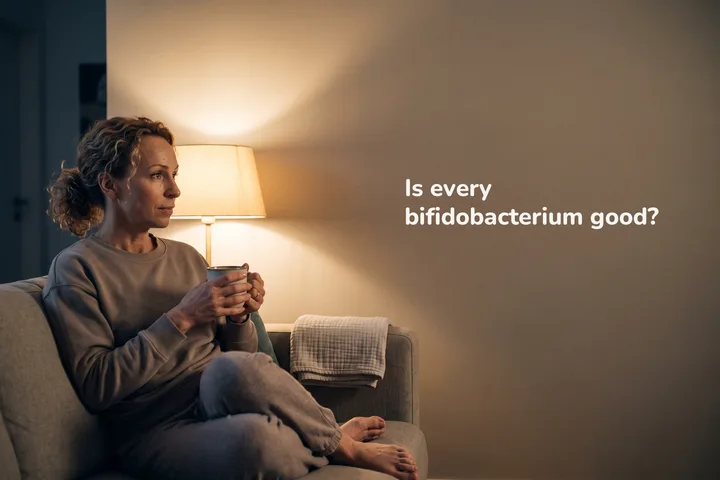 Is every bifidobacterium good? — a woman in her late twenties sits with a mug on the sofa in lamp light