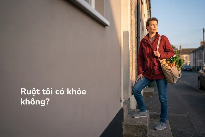 Ruột tôi có khỏe không? — một phụ nữ bước lên bậc thềm nhà lúc chiều tối, tay xách túi rau