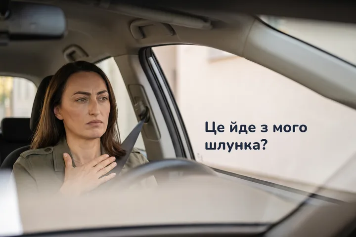Це йде з мого шлунка? — жінка у припаркованому авті серед ранку, долоня притиснута до живота